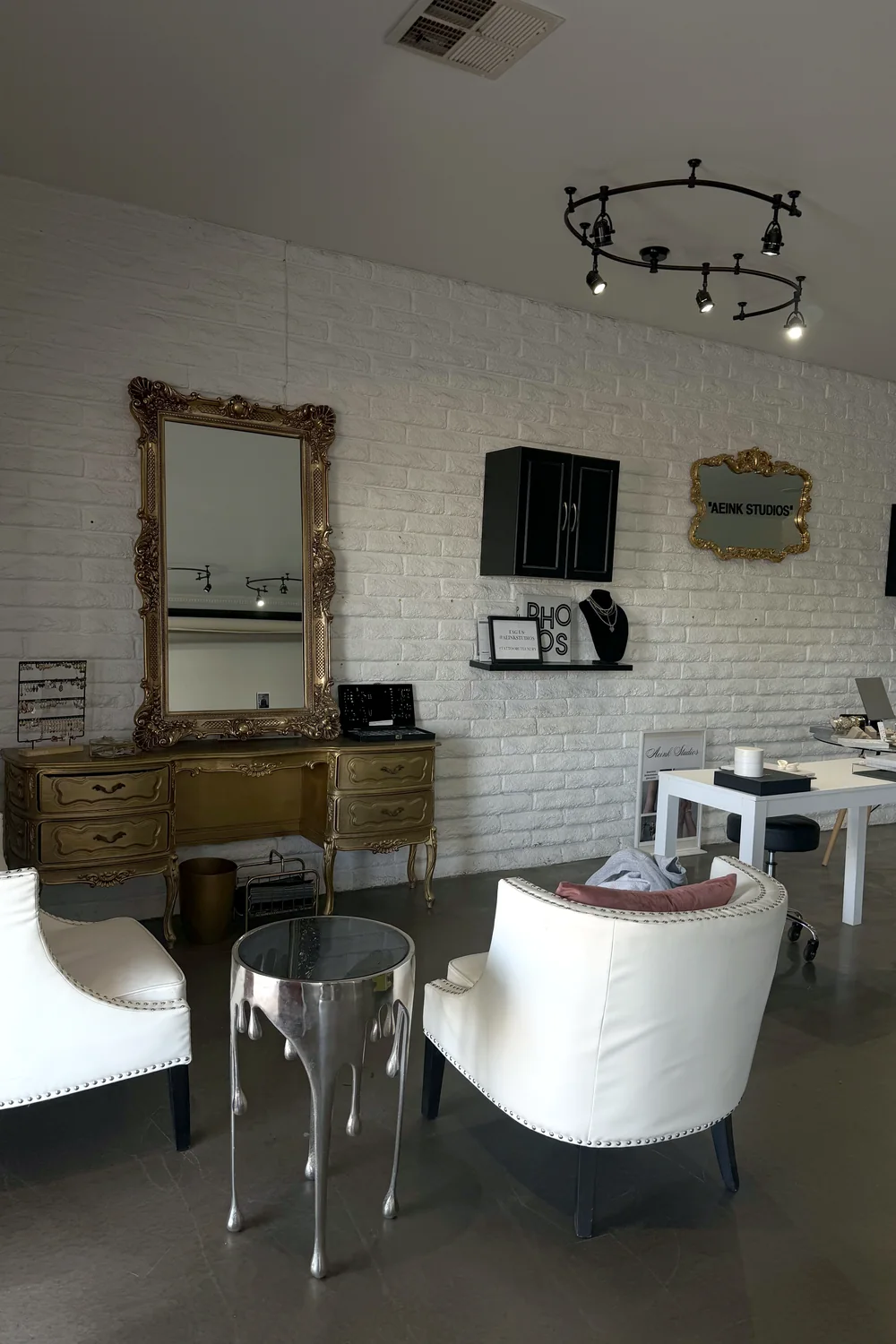 A gilded vanity and ornate mirror against the studio's white brick wall.