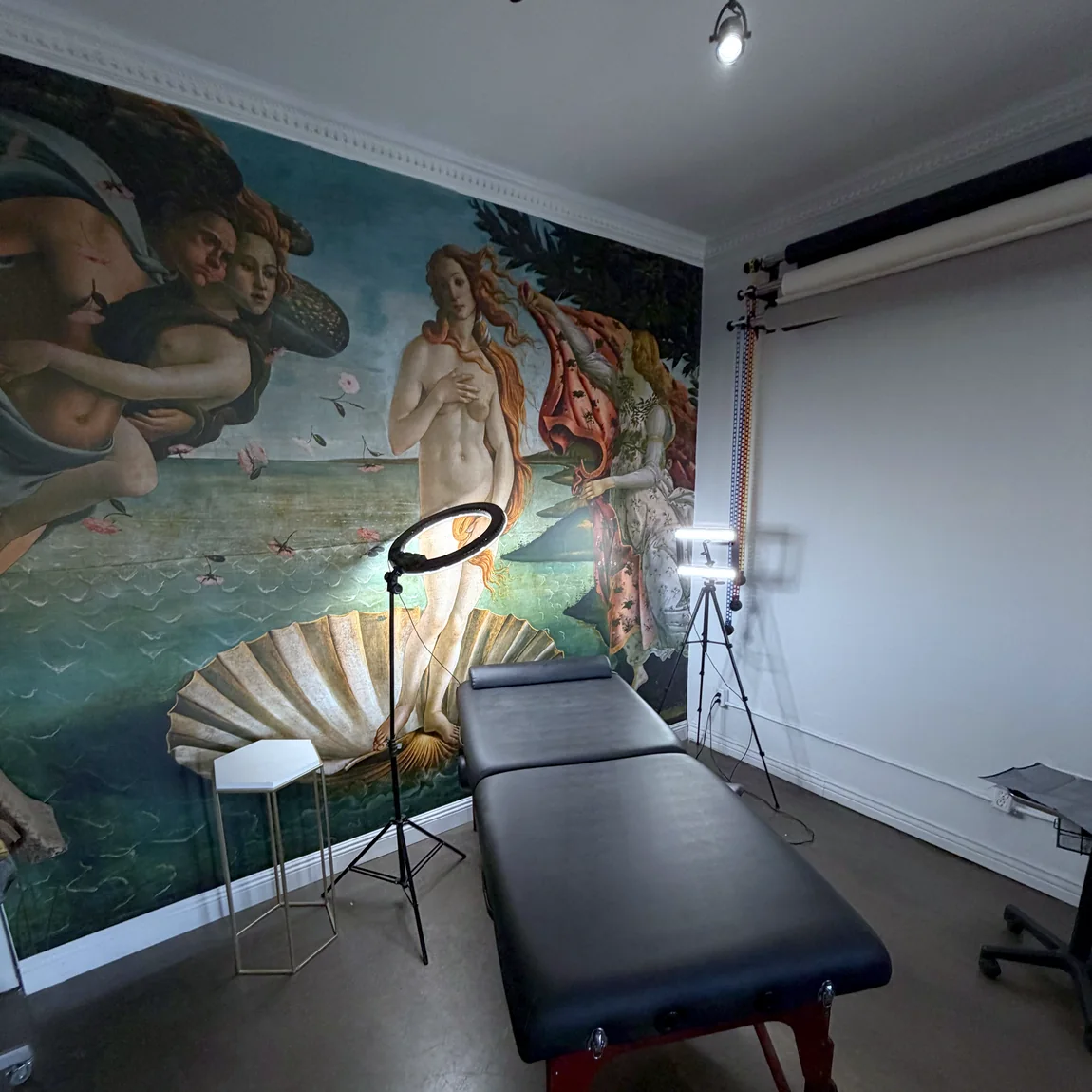 The AEInked treatment room, set against a full wall mural of Botticelli's Birth of Venus.