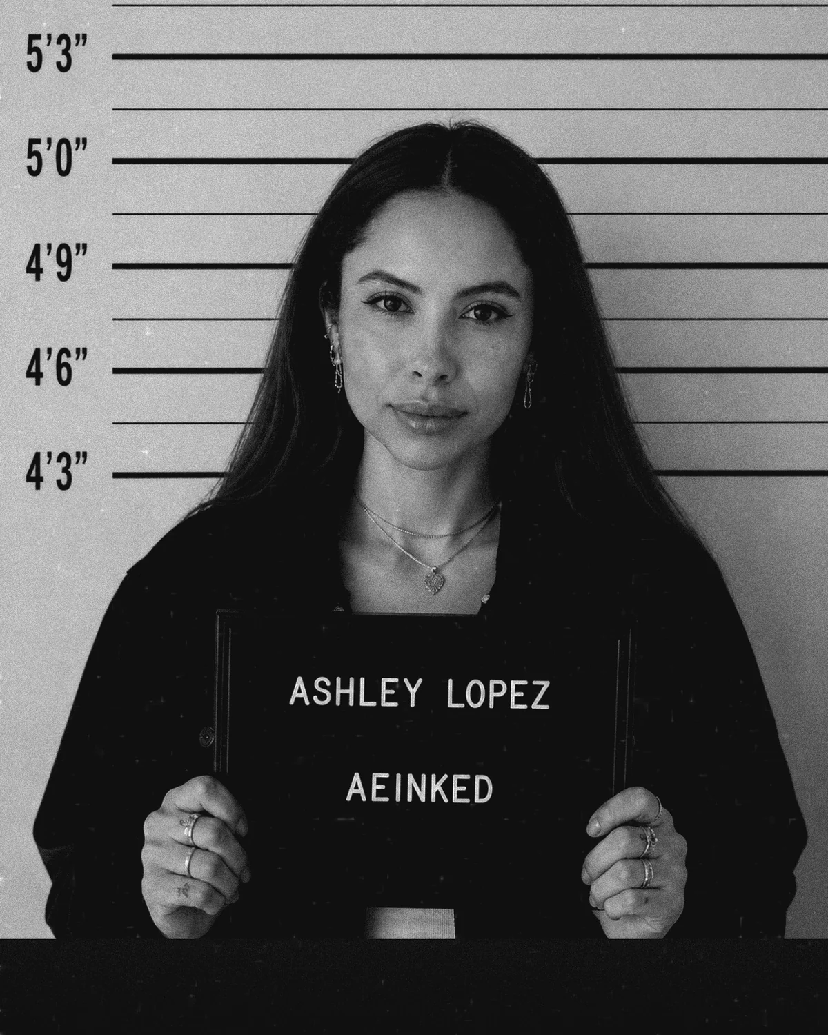 Ashley Lopez, founder and fine line artist at AEInked Studios, in a black and white mugshot-style portrait.