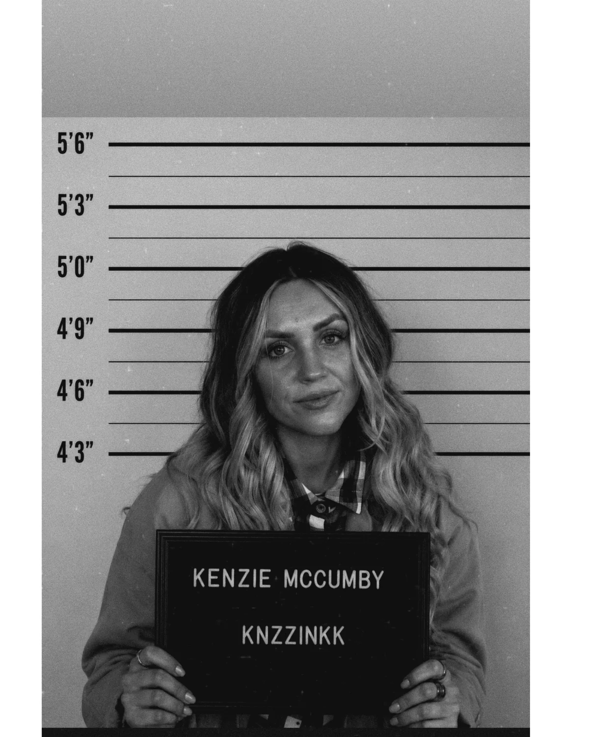 Kenzie McCumby, fine line tattoo artist at AEInked Studios, in a black and white mugshot-style portrait.