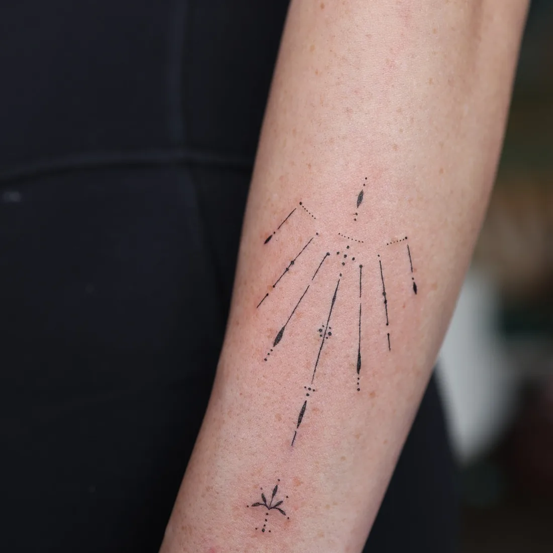 A fine line celestial burst tattooed on a forearm.