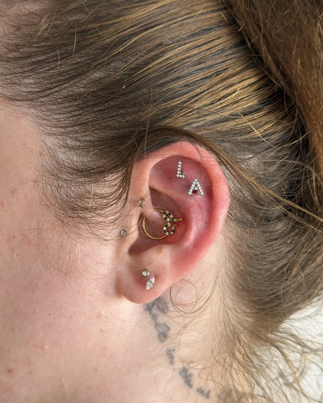 A curated ear with a gold cluster helix, studs and stacked lobes.