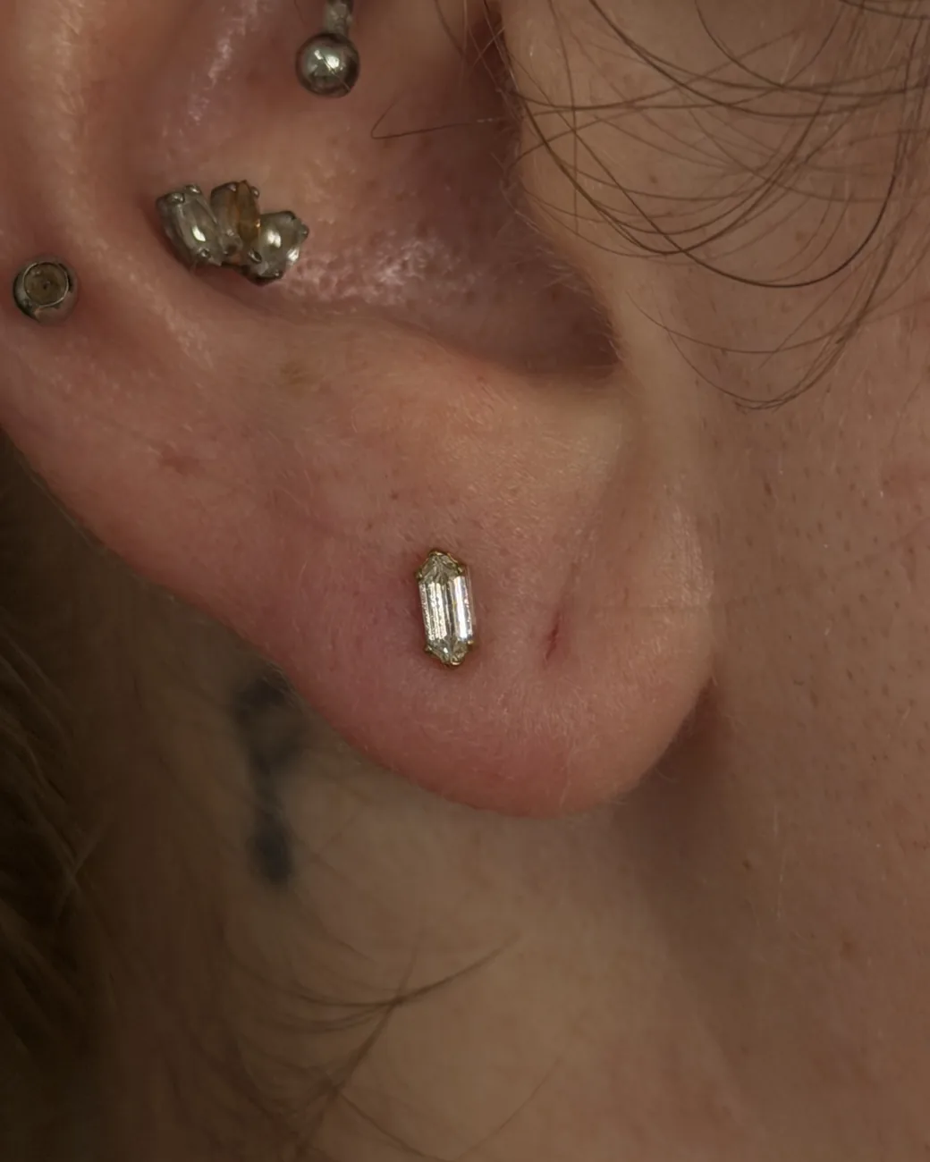 A close up of a baguette flat piercing and lobe studs in gold.