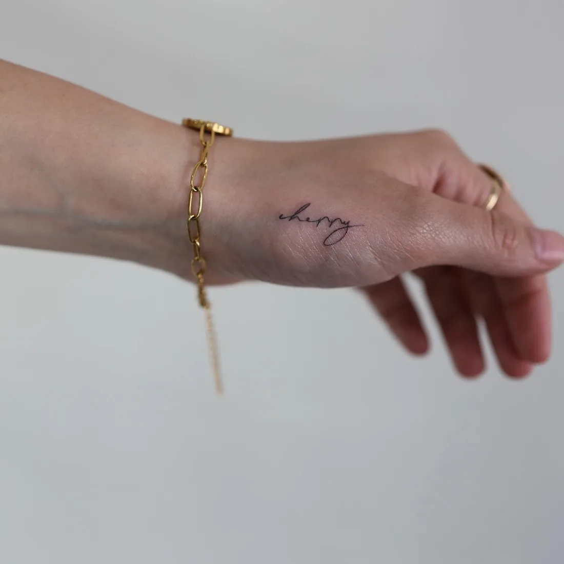 A short fine line word on the wrist, with a gold bracelet.