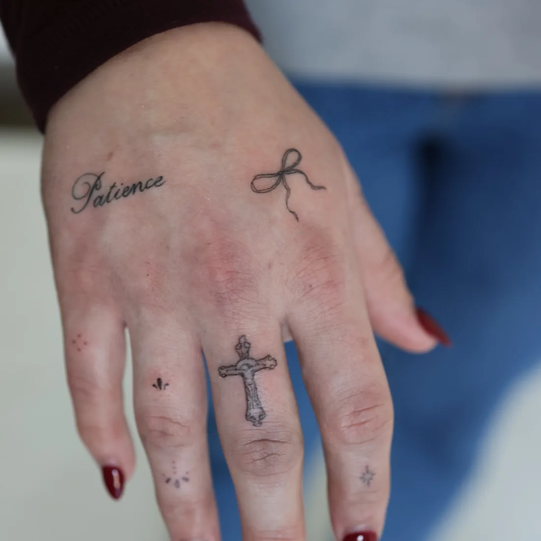 Fine line lettering, a bow and a cross tattooed across the fingers.
