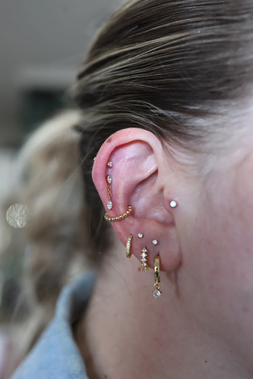 A fully curated ear with a gold cluster helix, conch and lobe piercings.