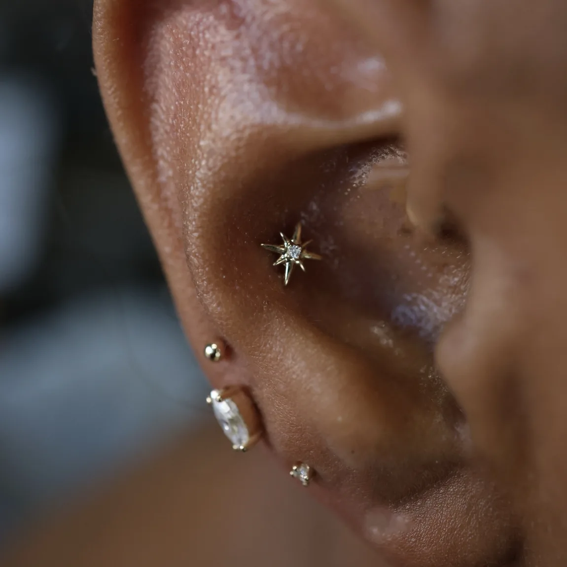 A close up of a gold starburst flat piercing with a baguette conch stud.